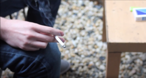 Photo of a hand holding a smoking cigarette inside a home