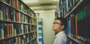 Photo of man looking at books on a library shelf